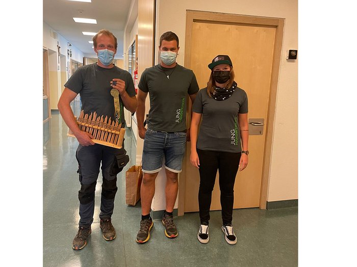 Eintauchen in die Welt der praktischen Berufe Drei Personen mit Masken stehen im Flur, eine hält ein Holzspielzeug