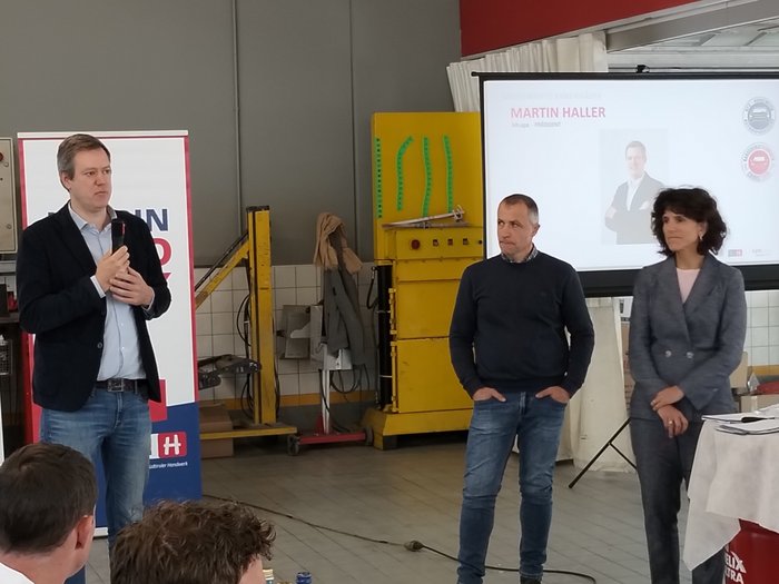 Assemblea annuale condivisa: confronto, innovazione e prospettive chiare Tre persone durante una presentazione in un'officina con pubblico presente