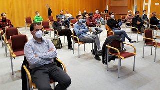 News Personen mit Masken sitzen mit Abstand in einem Seminarraum