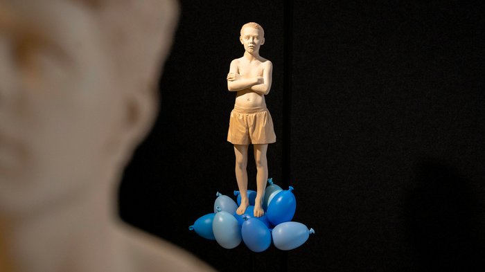 La 31^ Fiera d’Arte UNIKA apre le porte a Ortisei Scultura di un ragazzo in pantaloncini su palloncini blu con sfondo nero