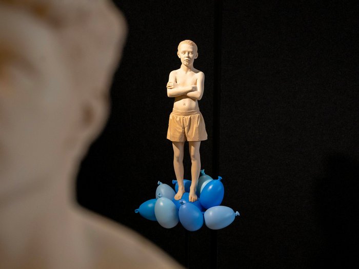 La 31^ Fiera d’Arte UNIKA apre le porte a Ortisei Scultura di un ragazzo in pantaloncini su palloncini blu con sfondo nero