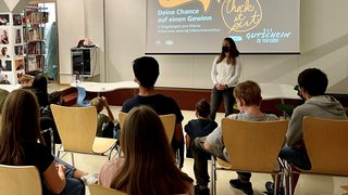 News Schülerin präsentiert vor Klasse, Text über Gewinnchance und Gutschein auf Leinwand