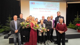 News Gruppenfoto bei Weihnachtsfeier mit Blumensträußen und Präsentation im Hintergrund