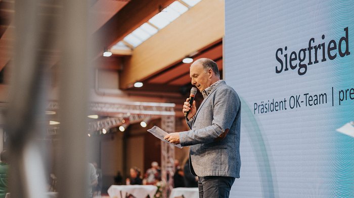 Erfolgreiche Eröffnung der Eisacktaler Wirtschaftsschau in Brixen – Ein Schaufenster der lokalen Wirtschaftskraft Mann hält Mikrofon und liest von Papier bei Event mit Präsentationswand