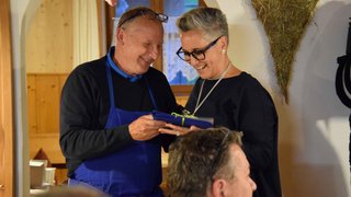 News Mann im blauen Schürze übergibt Frau lachend ein Geschenk