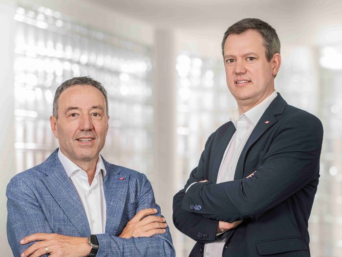 Neuerungen im öffentlichen Auftragswesen: Chancen für Südtirols Handwerksbetriebe Zwei Männer in Anzügen mit verschränkten Armen stehen vor hellem Hintergrund