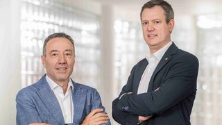 News Zwei Männer in Anzügen mit verschränkten Armen stehen vor hellem Hintergrund