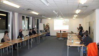 News Personen mit Masken bei einer Präsentation in einem hellen Konferenzraum