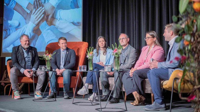 “Artigiani. Mani e Cuore” Sei persone sedute su un palco per una tavola rotonda con piante sui tavoli