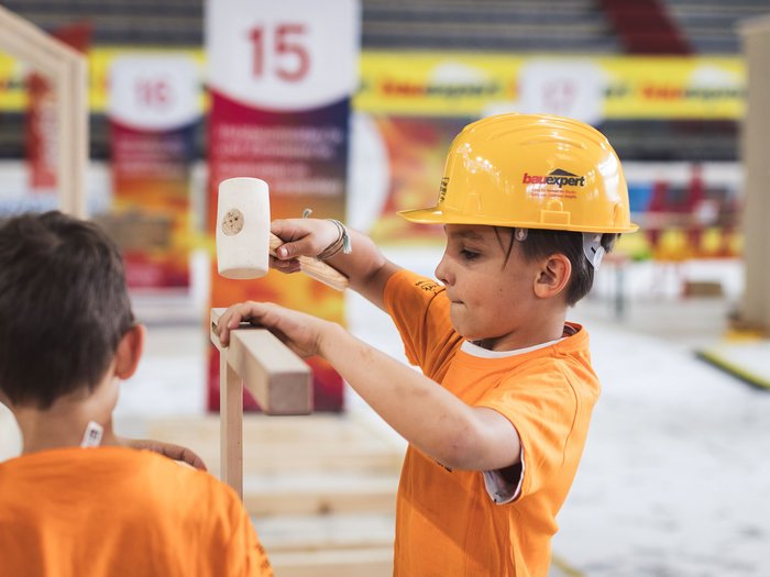 „Abenteuer Handwerk“ begeistert in Meran: Junge Talente erleben das Handwerk hautnah Junge mit gelbem Helm hämmert Holz auf einer Baustelle