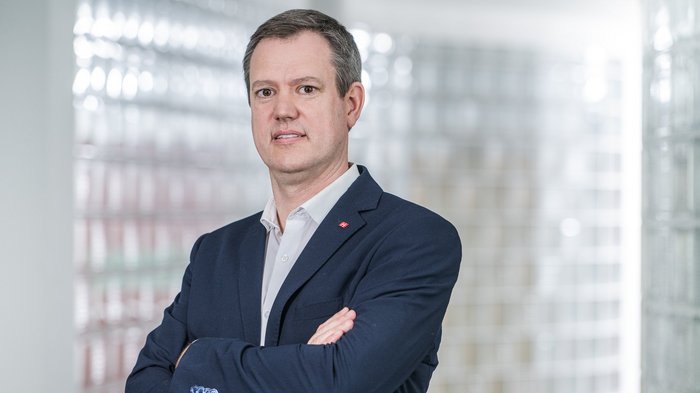 Werbesteuer in Südtirol: lvh begrüßt angekündigte Verbesserungen Geschäftsmann in Anzug steht mit verschränkten Armen vor glasigem Hintergrund