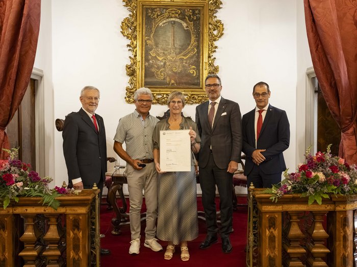 Premio Economia 2026: premiate 8 aziende associate lvh.apa Cinque persone in abiti formali tengono un certificato in una stanza con dipinto e tende rosse