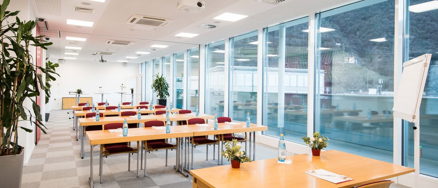 Affitto aule seminari Sala formazione moderna con tavoli, sedie, bottiglie d'acqua e grandi finestre