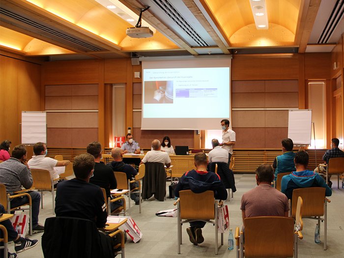Riscaldare all’insegna della sicurezza Persone sedute distanziate in una sala conferenze durante una presentazione.