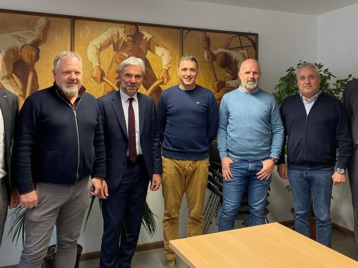 Il settore delle costruzioni richiede un adeguamento dei prezzi Sette uomini in piedi in un ufficio con un dipinto sullo sfondo