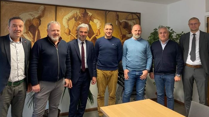 Il settore delle costruzioni richiede un adeguamento dei prezzi Sette uomini in piedi in un ufficio con un dipinto sullo sfondo