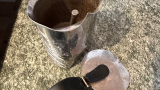 News Offener alter Metall-Kaffeebereiter mit schwarzem Griff auf einer grauen Arbeitsplatte