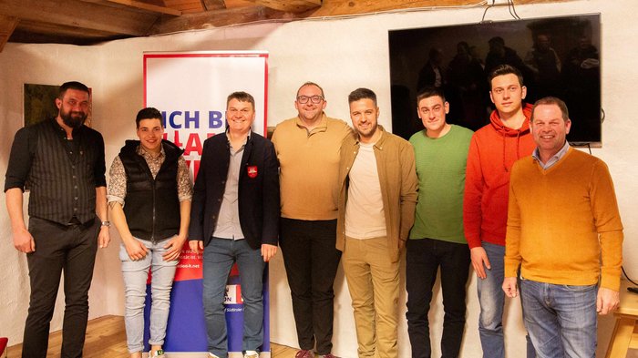 In programma c’è il futuro Otto uomini sorridenti posano in una stanza con soffitto in legno e banner