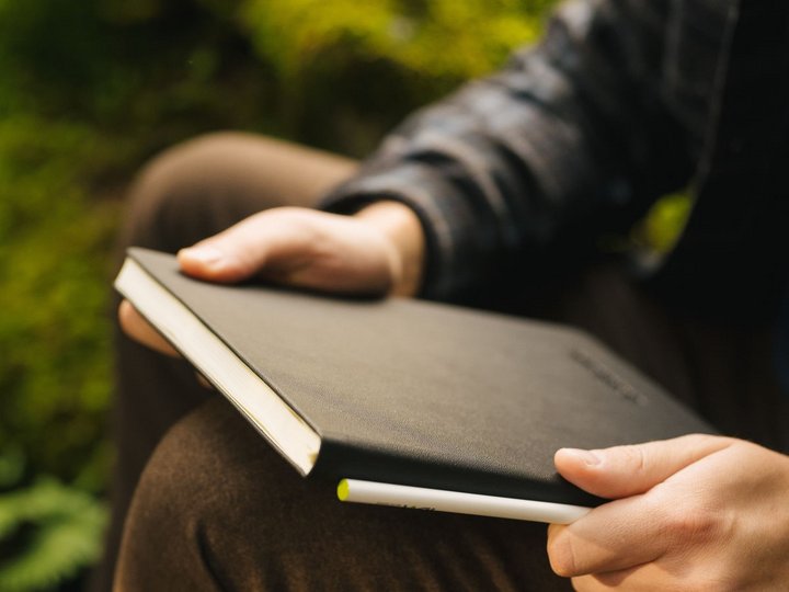 Das Nachhaltigkeitslabel Südtirol Person hält ein schwarzes Notizbuch und einen Stift im Freien