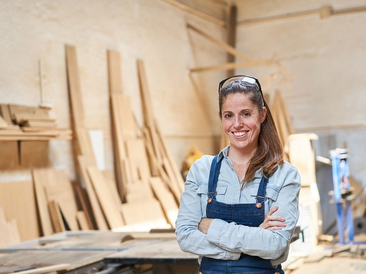 Lavorare deve convenire! Donna sorridente in officina con assi di legno sullo sfondo