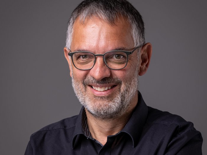 Großes Interesse für Öffentliche Aufträge im Pustertal Porträt eines lächelnden Mannes mit grauem Haar, Bart und Brille vor grauem Hintergrund