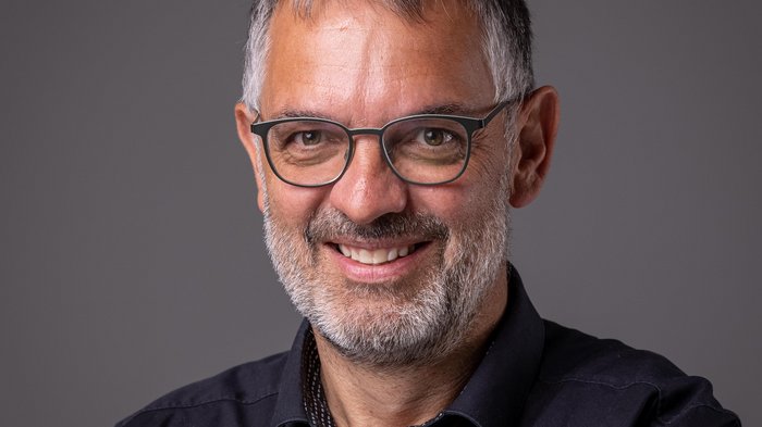 Grande interesse per gli appalti pubblici in Val Pusteria Ritratto di uomo sorridente con capelli grigi, barba e occhiali su sfondo grigio