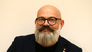 News Porträt eines lächelnden Mannes mit Brille und grauem Bart vor neutralem Hintergrund