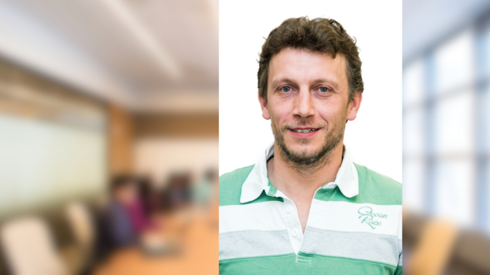 Una nuova e forte generazione di artigiani a Postal Ritratto di uomo sorridente con abbigliamento casual, sfondo ufficio sfocato