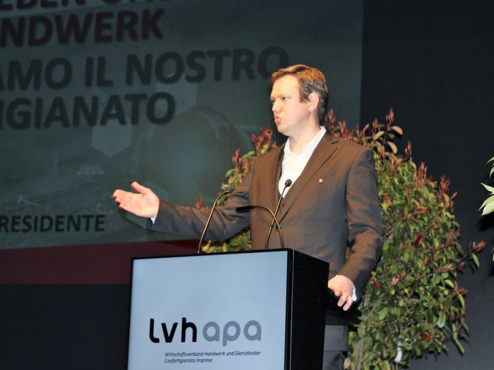 Landesversammlung des Südtiroler Handwerks Mann hält Vortrag auf Konferenz vor lvhapa Logo und Pflanzen