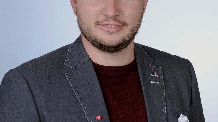 Imprese movimento terra: i prezzi dei combustibili sono insostenibili Ritratto di uomo sorridente con barba, giacca grigia e maglietta rossa su sfondo neutro