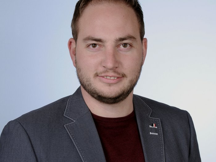 Imprese movimento terra: la sfida principale è l’aumento dei prezzi Ritratto di uomo sorridente con barba, giacca grigia e maglietta rossa su sfondo neutro