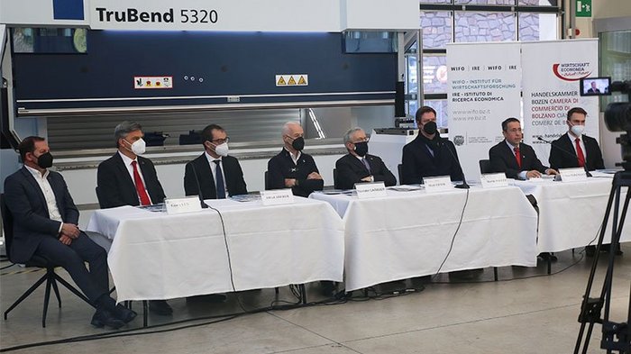 Handwerk in Südtirol: zwischen Tradition und Digitalisierung Sieben Männer mit Masken sitzen an einem langen Tisch vor Kamera in Fabrikumgebung