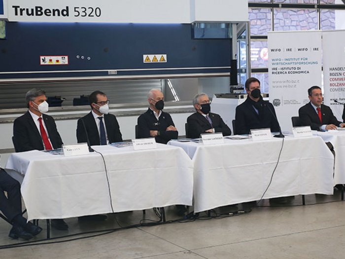 Handwerk in Südtirol: zwischen Tradition und Digitalisierung Sieben Männer mit Masken sitzen an einem langen Tisch vor Kamera in Fabrikumgebung