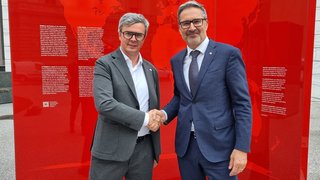 News Zwei Männer in Anzügen schütteln vor roter Weltkarte Hände