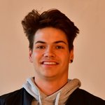 Bozen Land Junger Mann mit dunklen Haaren und Kapuzenpullover lächelt vor beigem Hintergrund