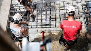 News Zwei Bauarbeiter mit Helmen montieren Stahlarmierung auf einer Baustelle