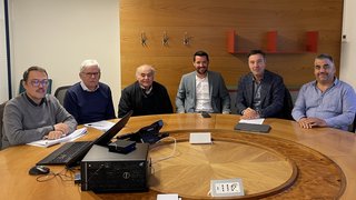 News Sechs Männer in einem Konferenzraum an einem runden Holztisch sitzen