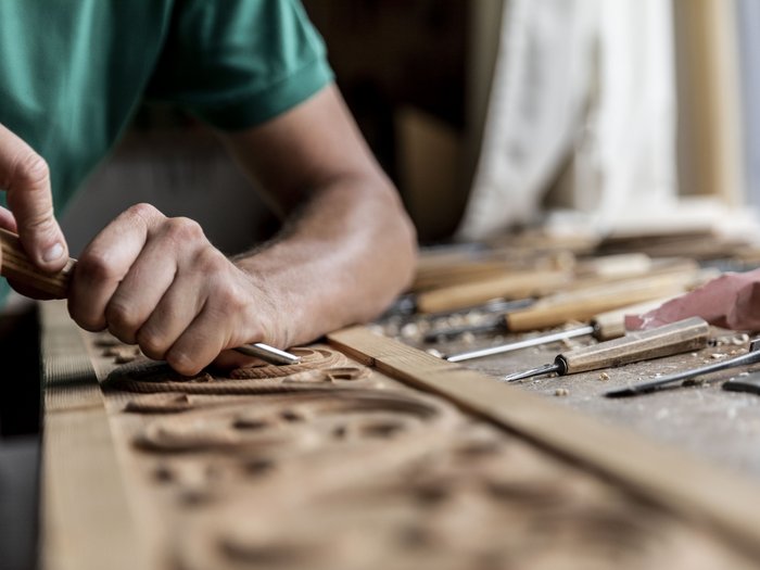 L’artigianato artistico di lvh.apa compie 75 anni Artigiano intaglia decorazioni in legno con scalpello sul banco da lavoro