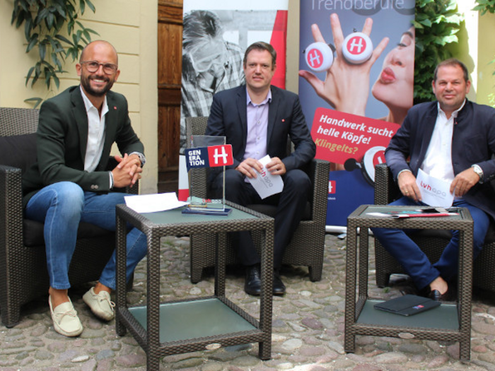 Resilienz und Adaptionsfähigkeit sind Stärken des Handwerks Drei Männer sitzen auf Rattanmöbeln vor Bannern bei einer Außenveranstaltung