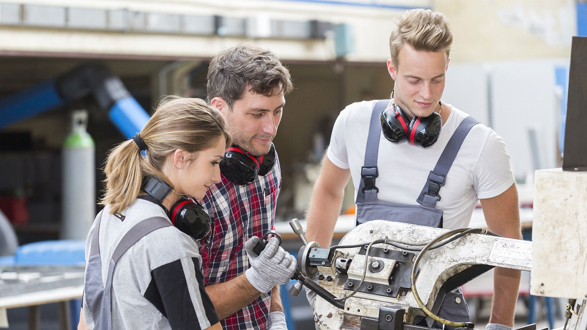 Home Tre apprendisti lavorano con una macchina di metallo in una officina