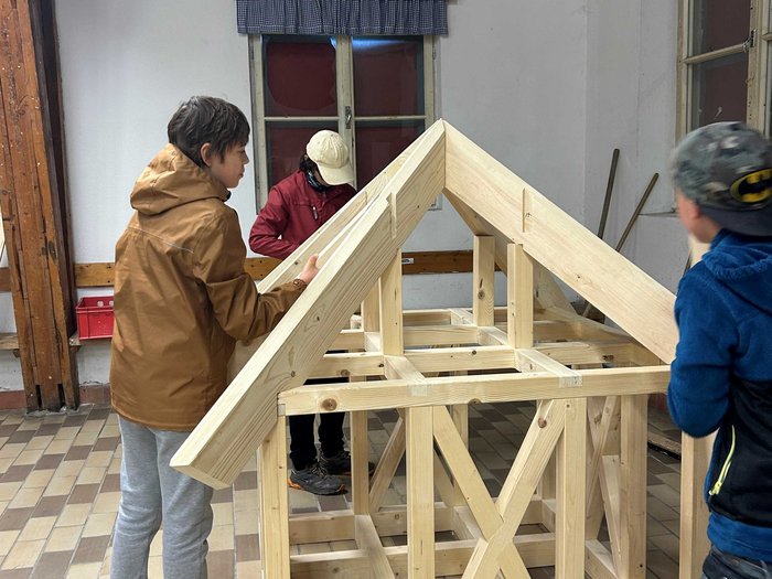 JHW-Wipptal Drei Kinder bauen ein Gerüst aus Holz für ein kleines Haus im Innenraum