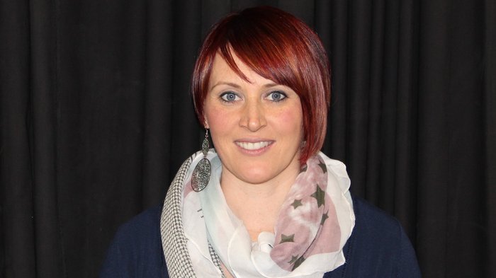 „Es wird Zeit, dass wir wieder aufsperren dürfen!“ Frau mit rotem Kurzhaarschnitt und gemustertem Schal vor schwarzem Hintergrund