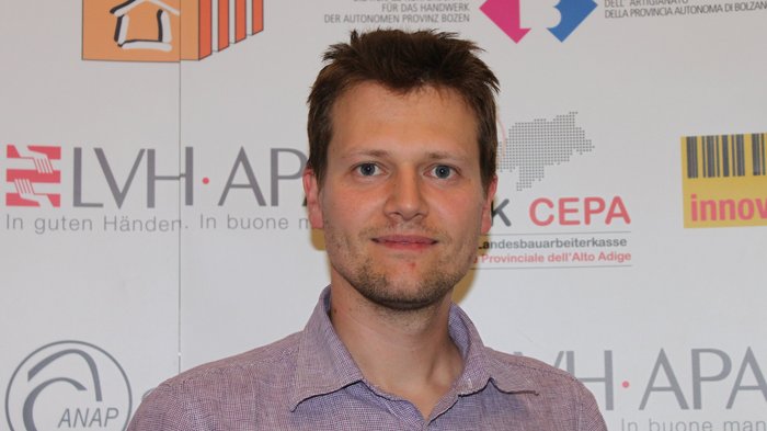 Revisionen aufgeschoben, frühzeitiger Termin dennoch wichtig Porträt eines Mannes vor einer Wand mit Logos und Texten in Deutsch und Italienisch