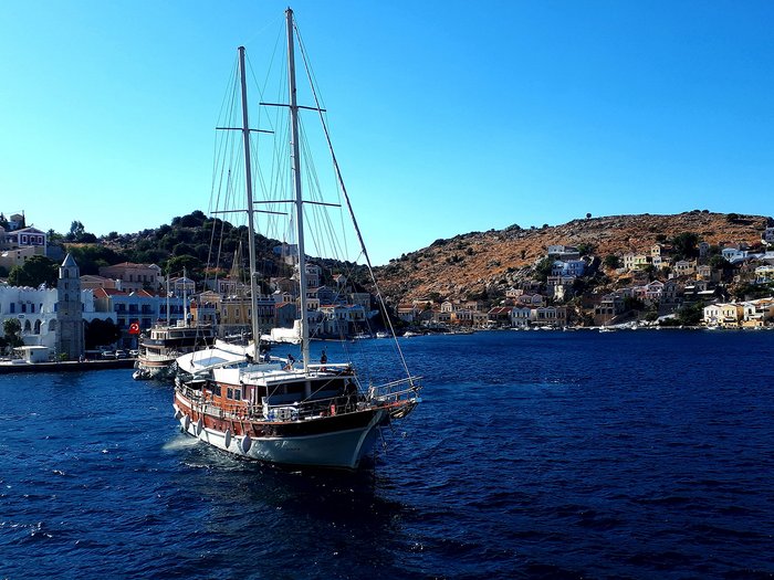 Althandwerker Rhodos 2022 © lvh.apa Segelboot auf blauem Meer vor einem Küstenort mit Häusern und Hügeln