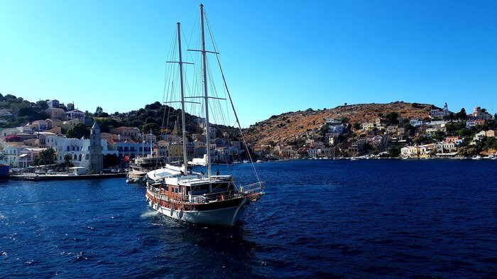 Althandwerker Rhodos 2022 © lvh.apa Segelboot auf blauem Meer vor einem Küstenort mit Häusern und Hügeln