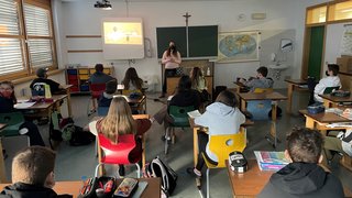 News Schüler sitzen in einem Klassenraum und hören einer Lehrerin mit Maske zu