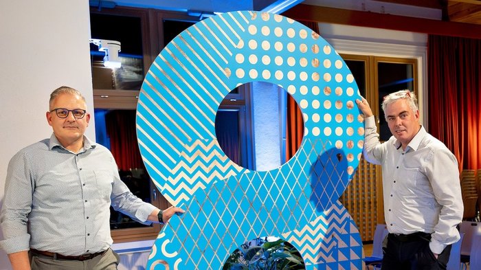 Rittner Musterschau verbindet Menschen und Ideen Zwei Männer stehen neben einer großen blauen 8 mit Mustern in einem Raum