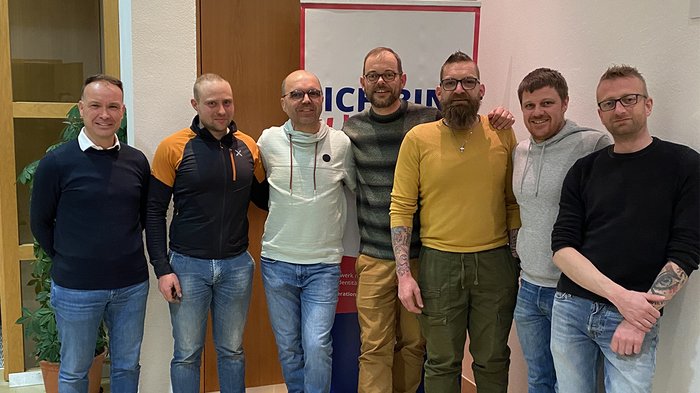 Handwerk verbindet Welten – Warum Shanghai näher ist, als man denkt Sieben Männer stehen vor einer Tür und einem Banner in Innenraum