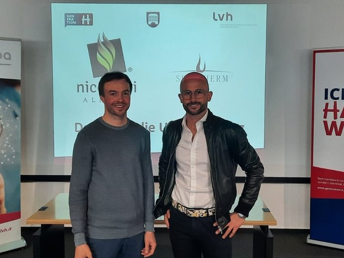 Großer Andrang beim Jahrestreffen der Hafner/innen Zwei Männer stehen vor einem Bildschirm und Bannern bei einer Handwerksveranstaltung.