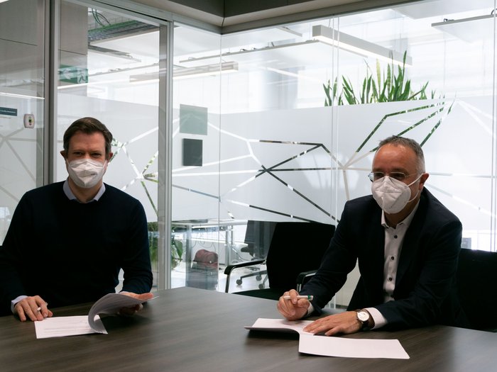 Kooperation zwischen lvh und Fraunhofer Italia verlängert Zwei Männer mit Schutzmasken sitzen an einem Tisch und unterzeichnen Dokumente in einem Büro